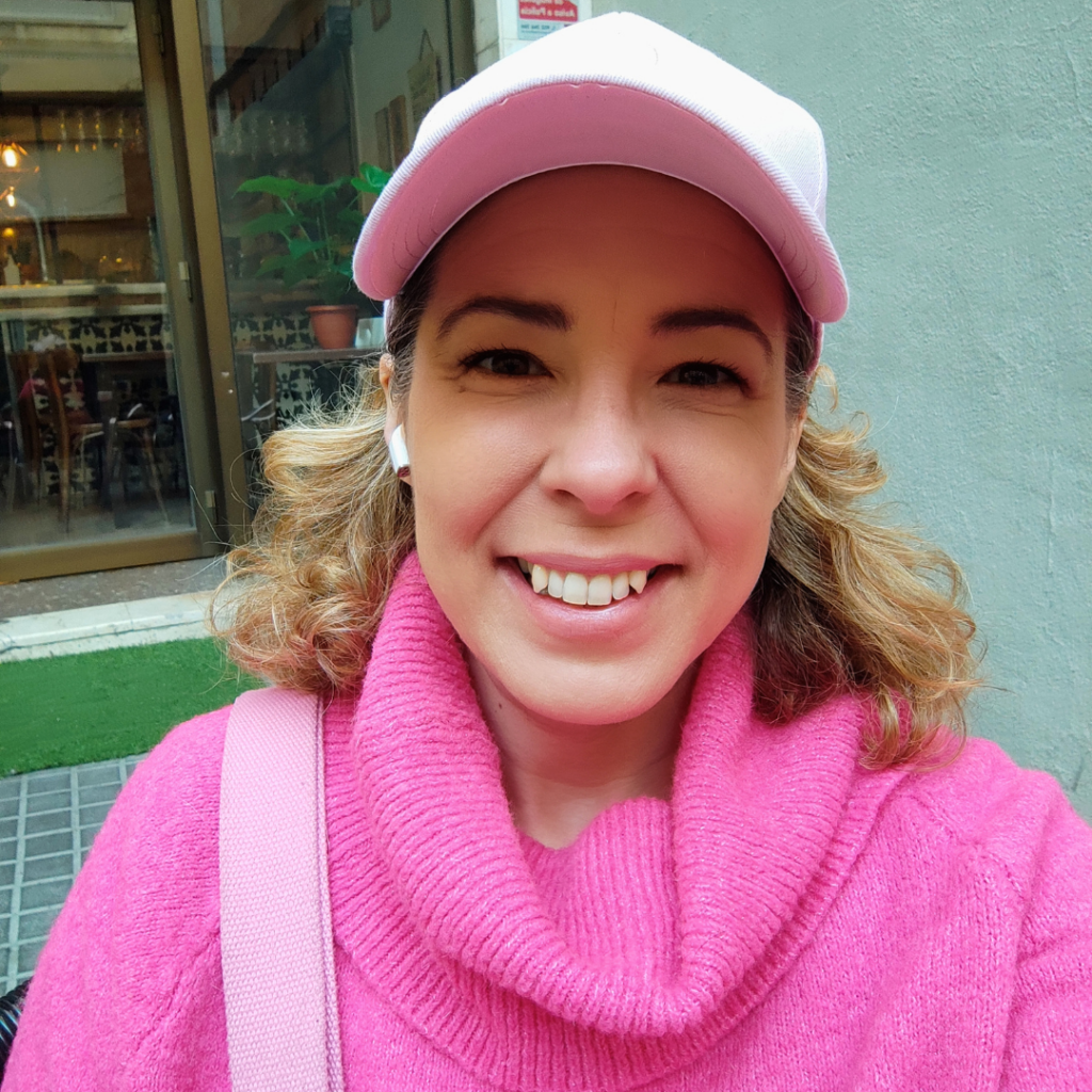 Headshot of Julia Zatta wearing a pink baseball cap and pink sweather. She is smiling and looking directly at the camera.